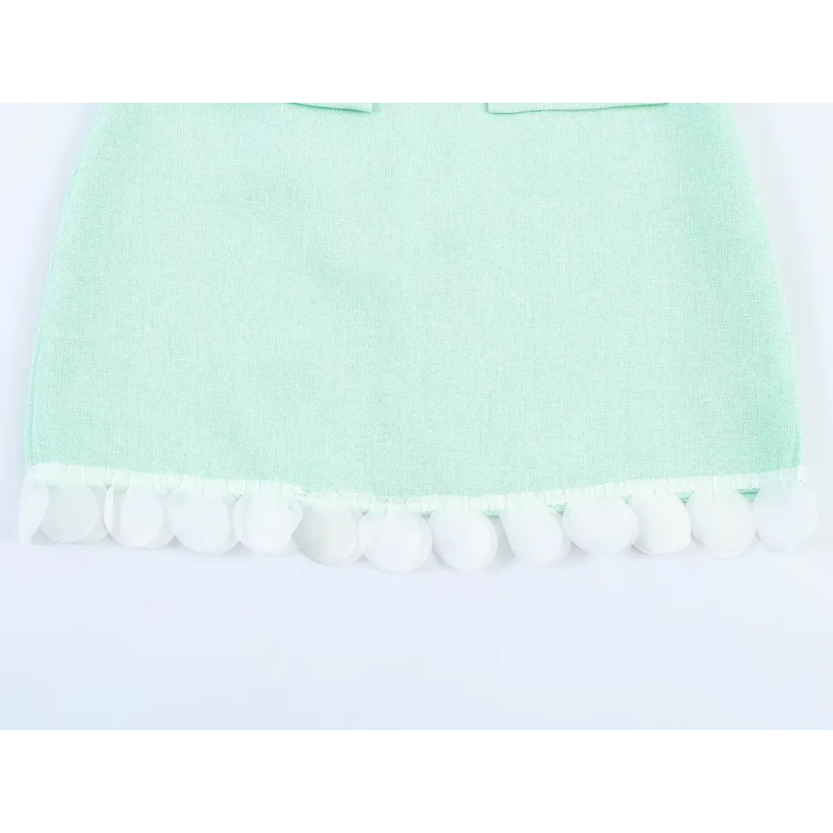 Close-up of the hem on a mint green tweed sleeveless dress, showcasing the decorative white petal-shaped trim.
