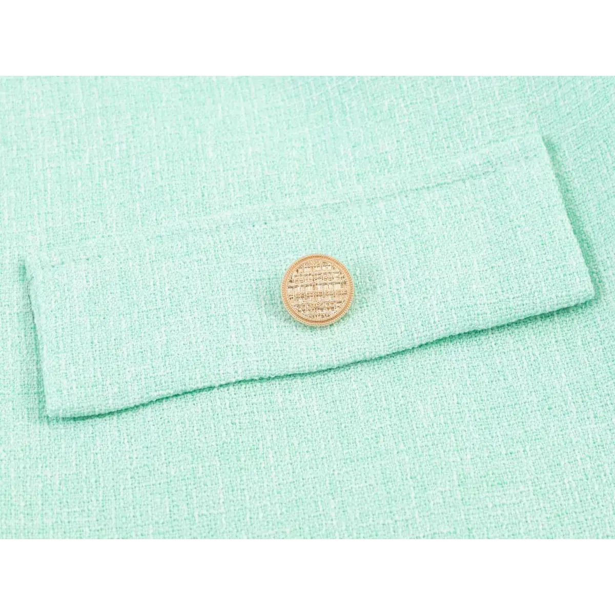 Close-up of a decorative pocket and textured gold button on a mint green tweed dress.
