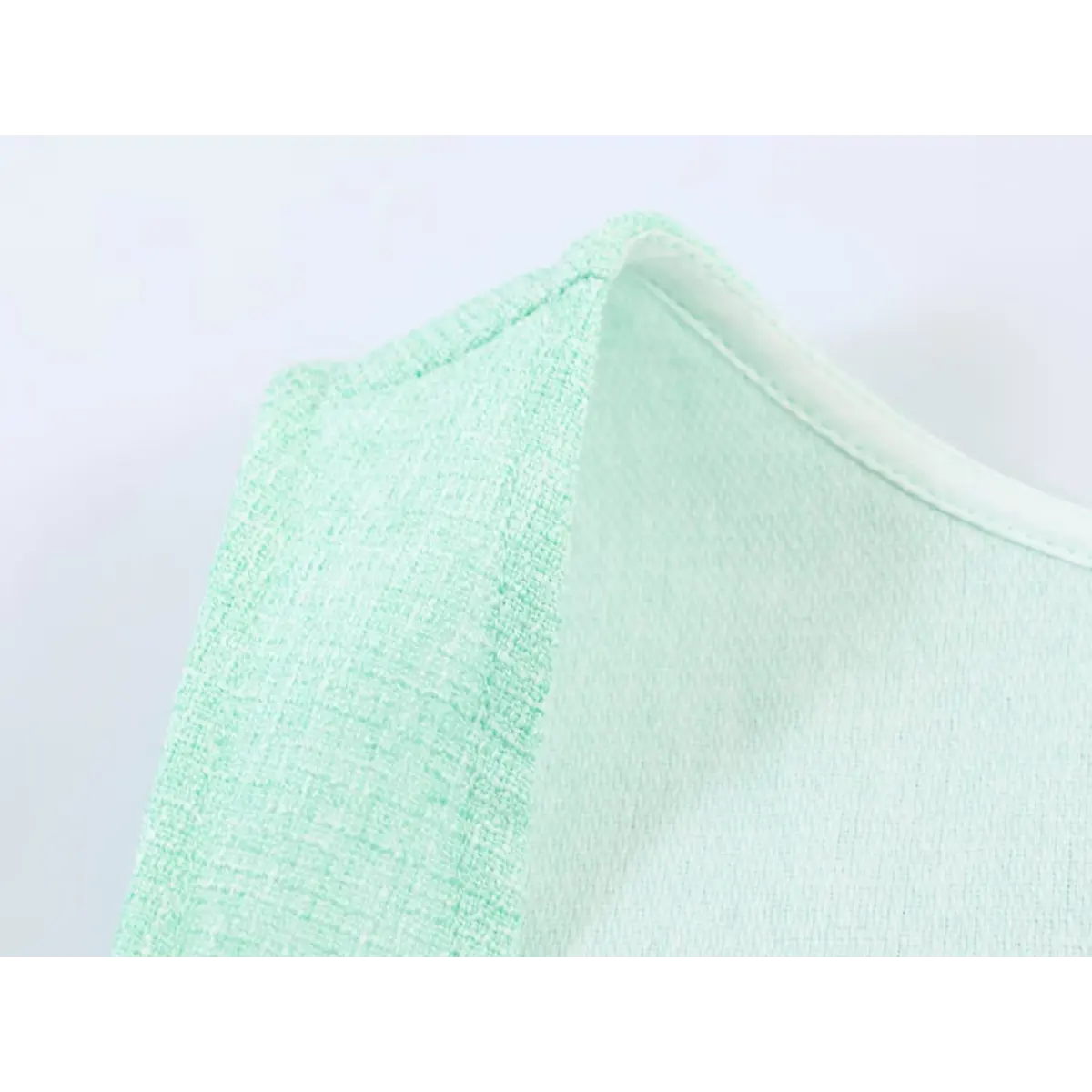 Close-up of the shoulder seam and fabric texture on a mint green tweed sleeveless dress.