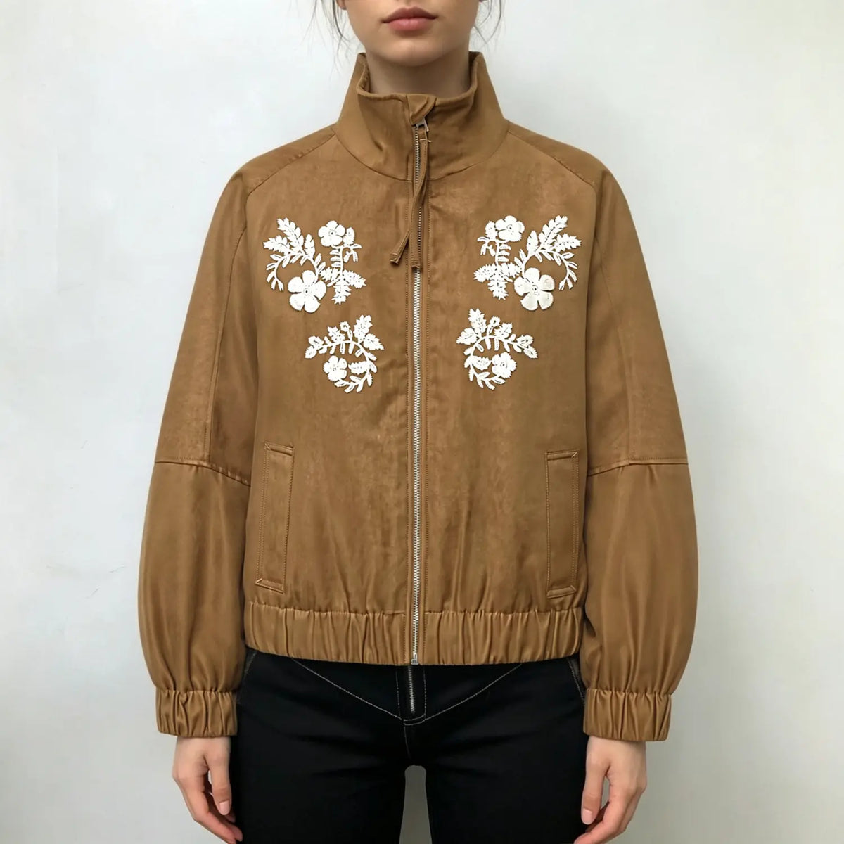 Female model wearing brown faux suede bomber jacket with white floral embroidery, front full view