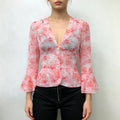 Model front view wearing pink watercolor floral chiffon peplum blouse, v‑neck pearl buttons, bell flare sleeves, paired with black pants
