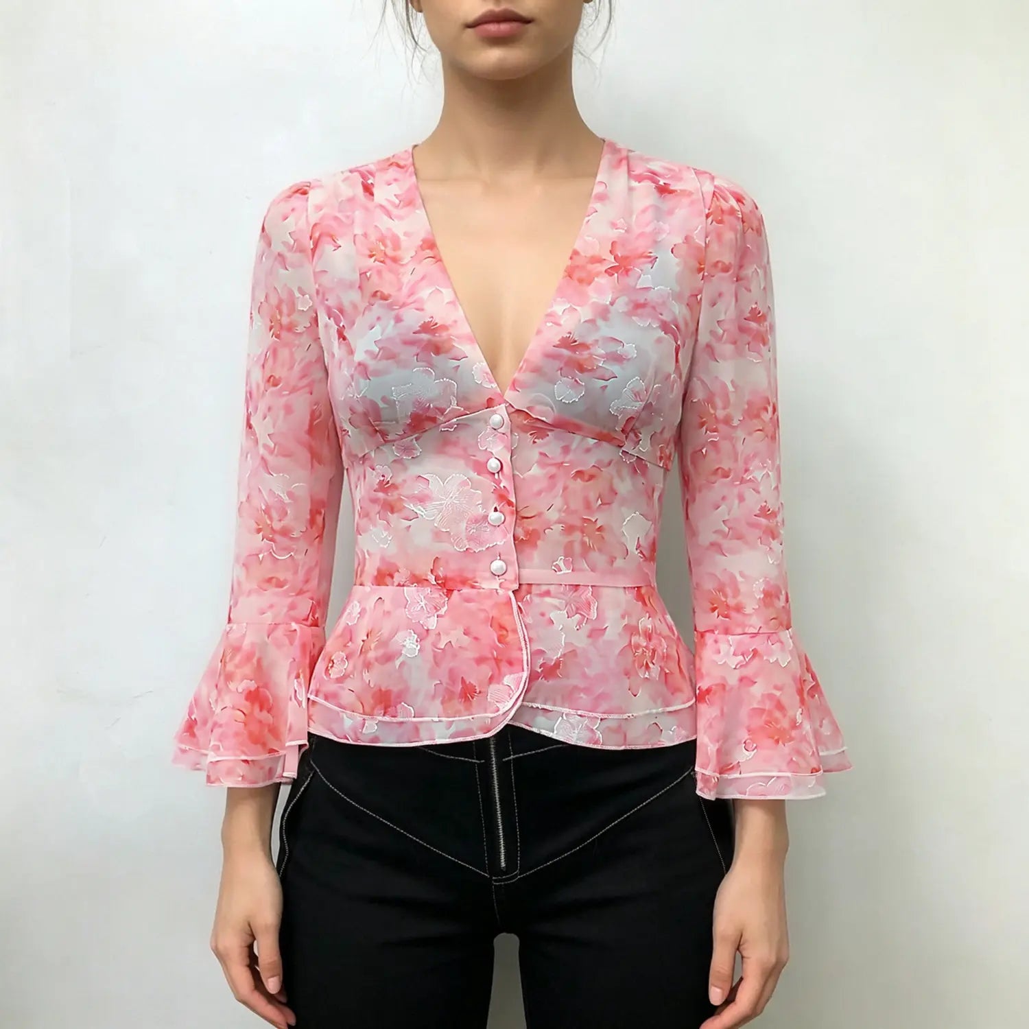 Model front view wearing pink watercolor floral chiffon peplum blouse, v‑neck pearl buttons, bell flare sleeves, paired with black pants