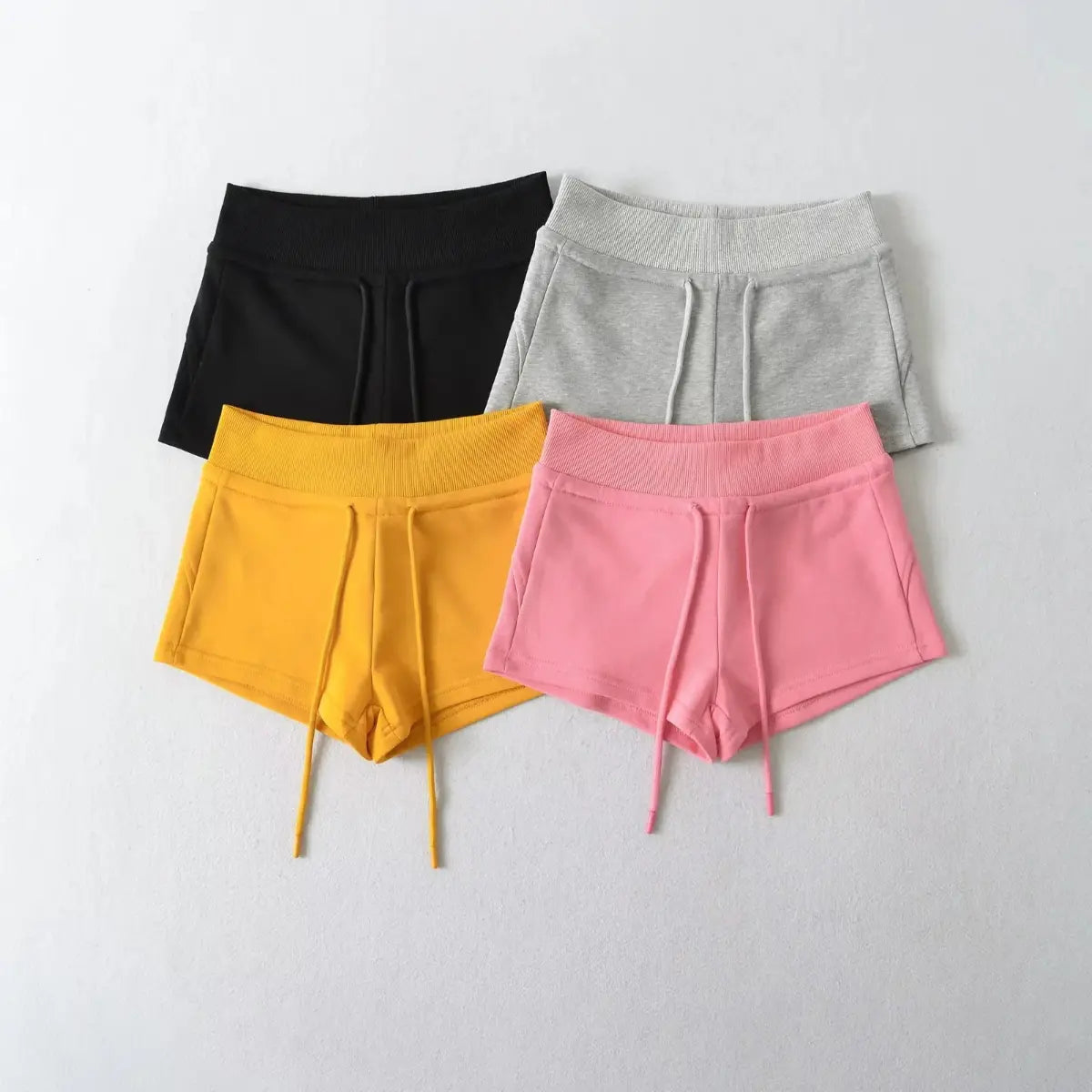 Flat lay view of high-waisted drawstring shorts in black, grey, yellow, and pink.