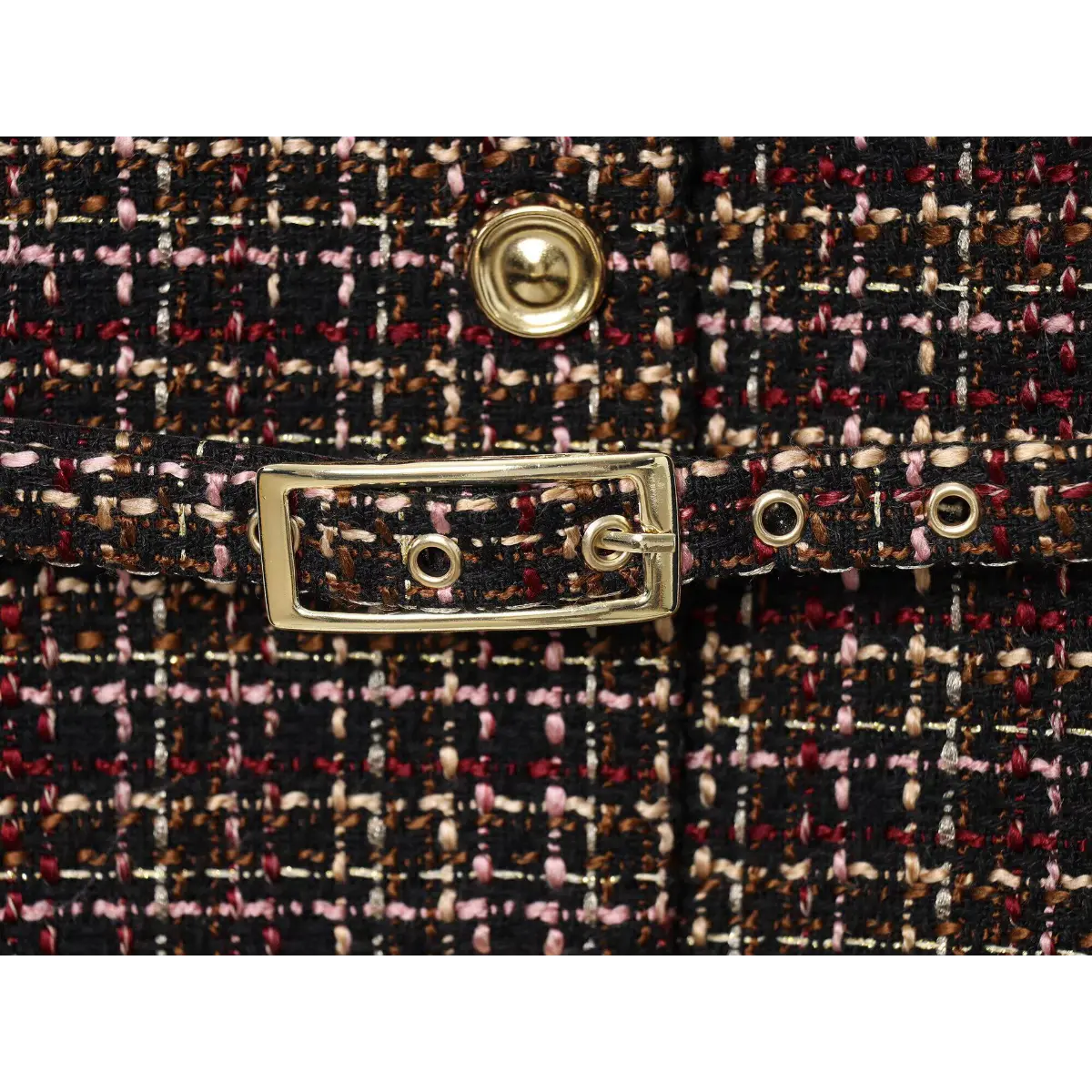 Close-up of the gold-tone belt buckle on the tweed tunic, showing the eyelets and matching fabric