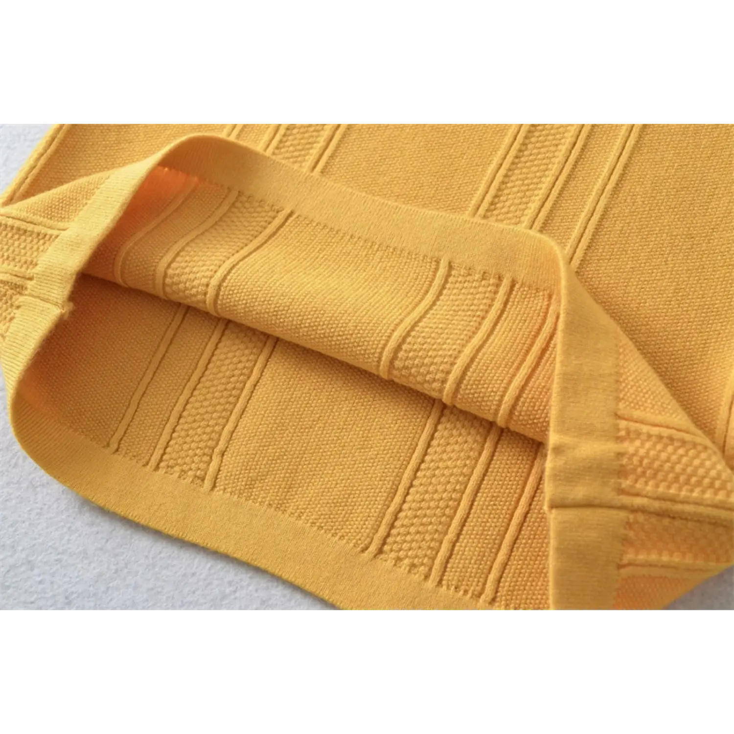 Mustard yellow ribbed knit fabric double fold macro flat shot, bumpy vertical stripe stretch knit texture white background detail