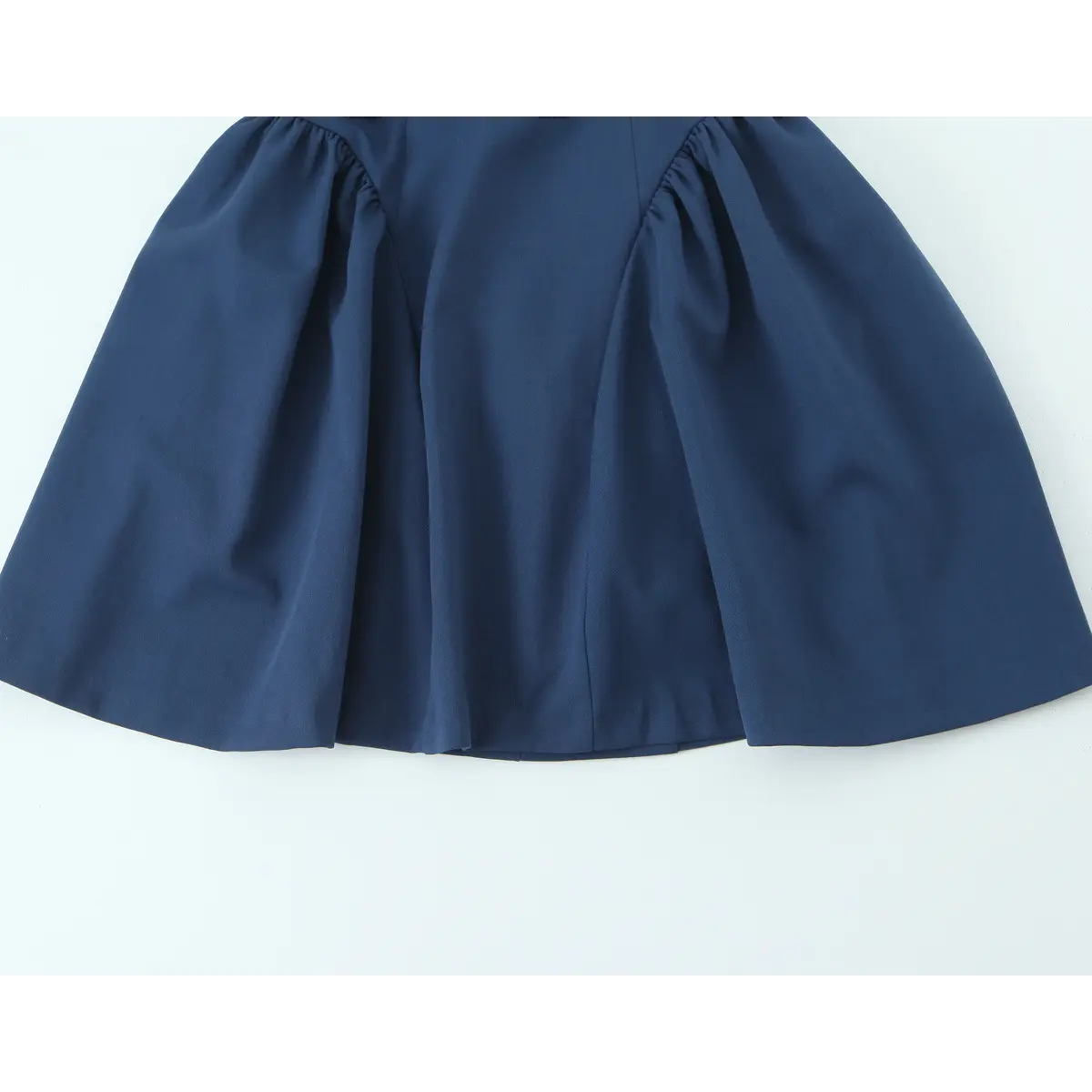 Close-up detail of the flared skirt hem and finished edge on a navy blue halter-neck mini dress.