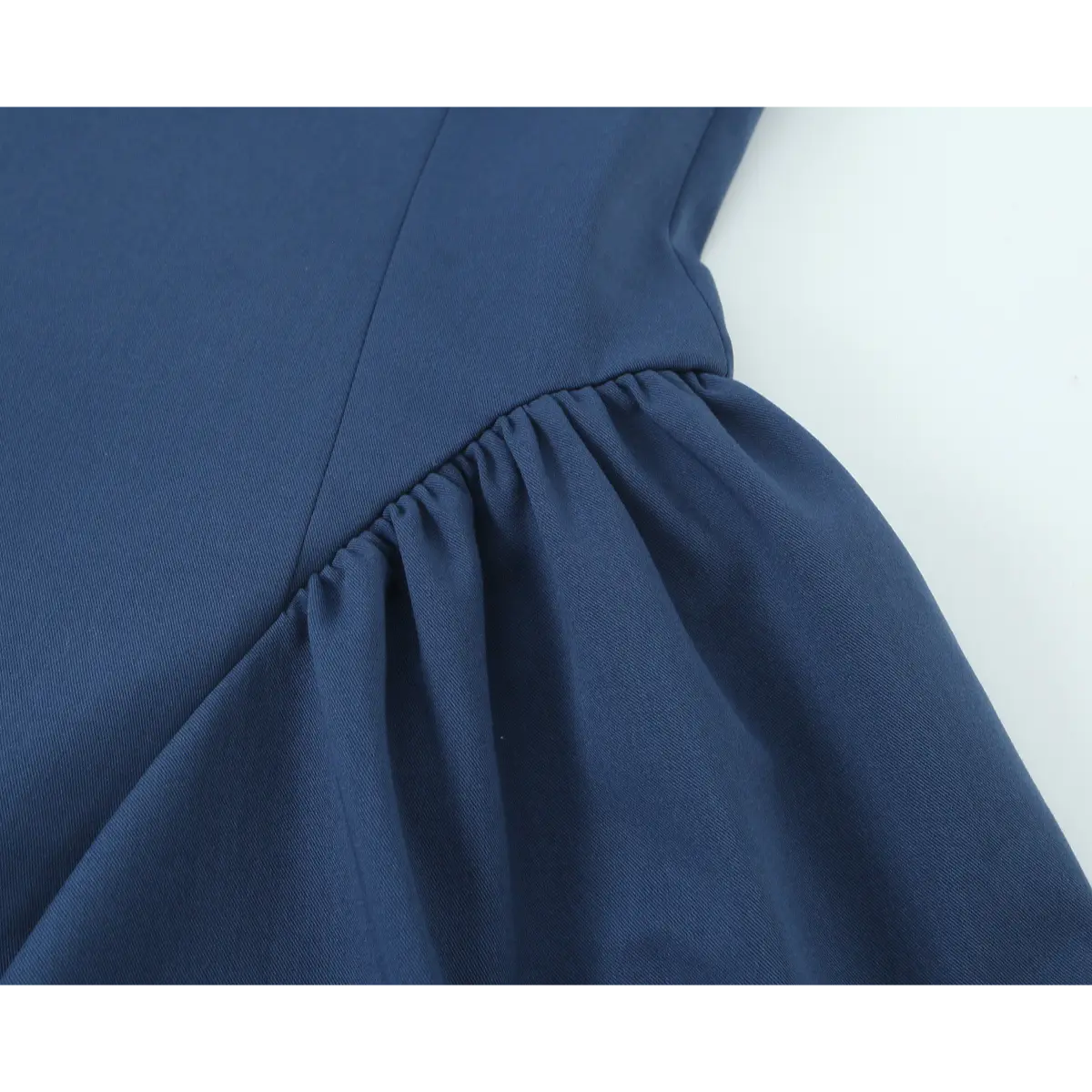 Close-up detail of the gathered waist seam on a navy blue halter-neck mini dress, showing the transition to the flared skirt.