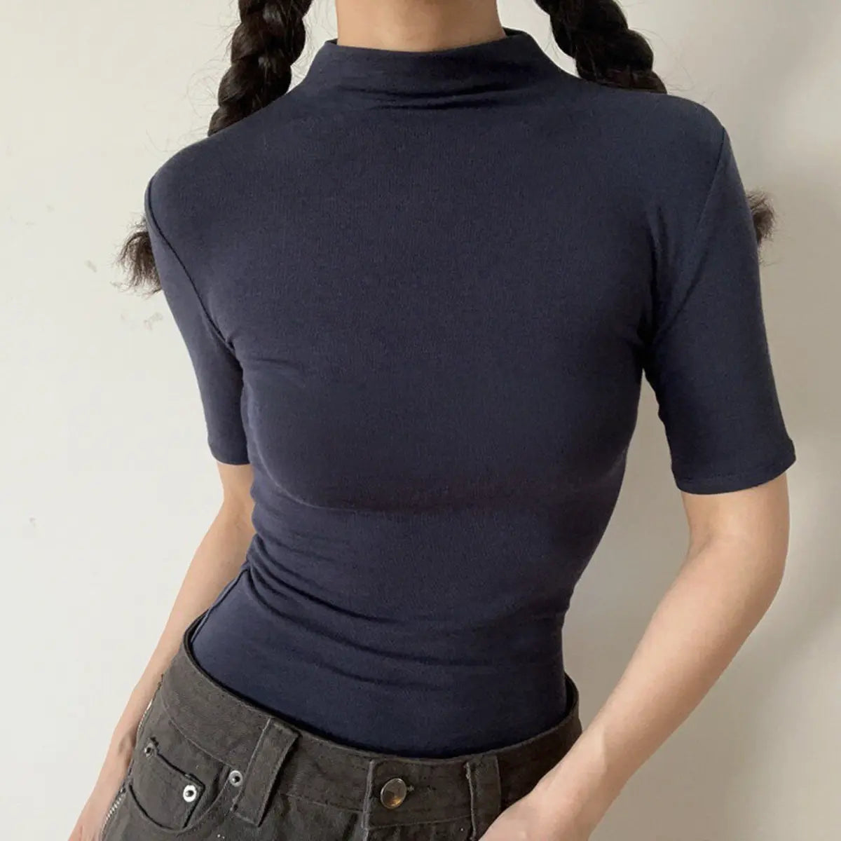 Lifestyle shot of form-fitting navy blue ribbed half-turtleneck short-sleeve top, tucked into jeans