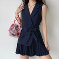 Model wearing navy blue sleeveless blazer belted pleated mini dress with pearl necklace and pink bag