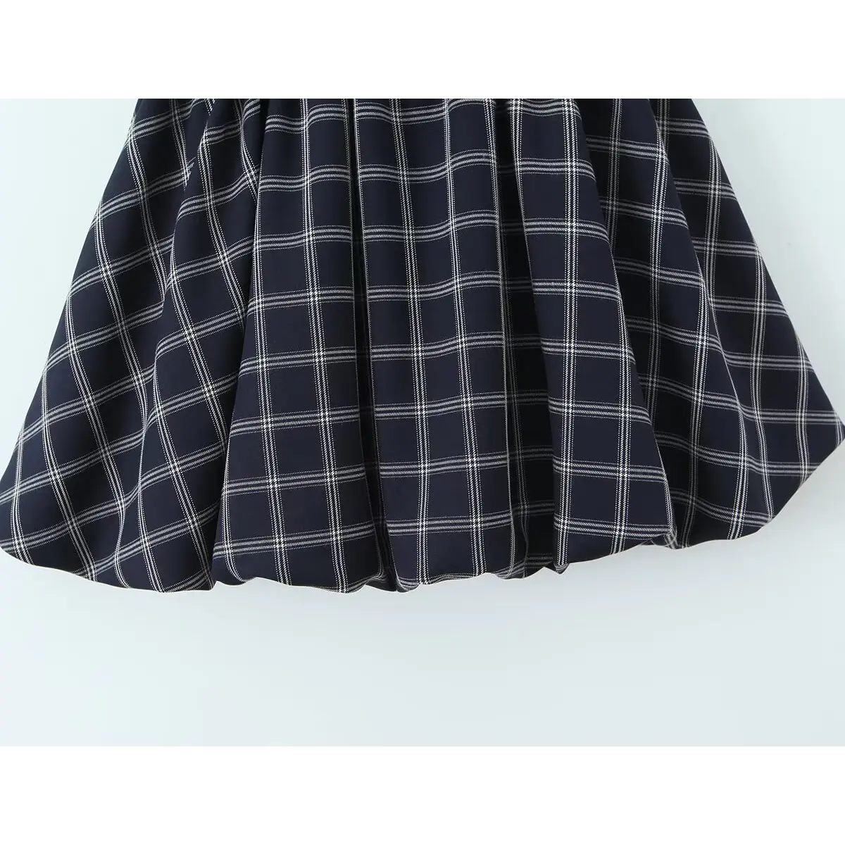 Close-up of the gathered skirt hem and checkered fabric texture on the navy cami dress