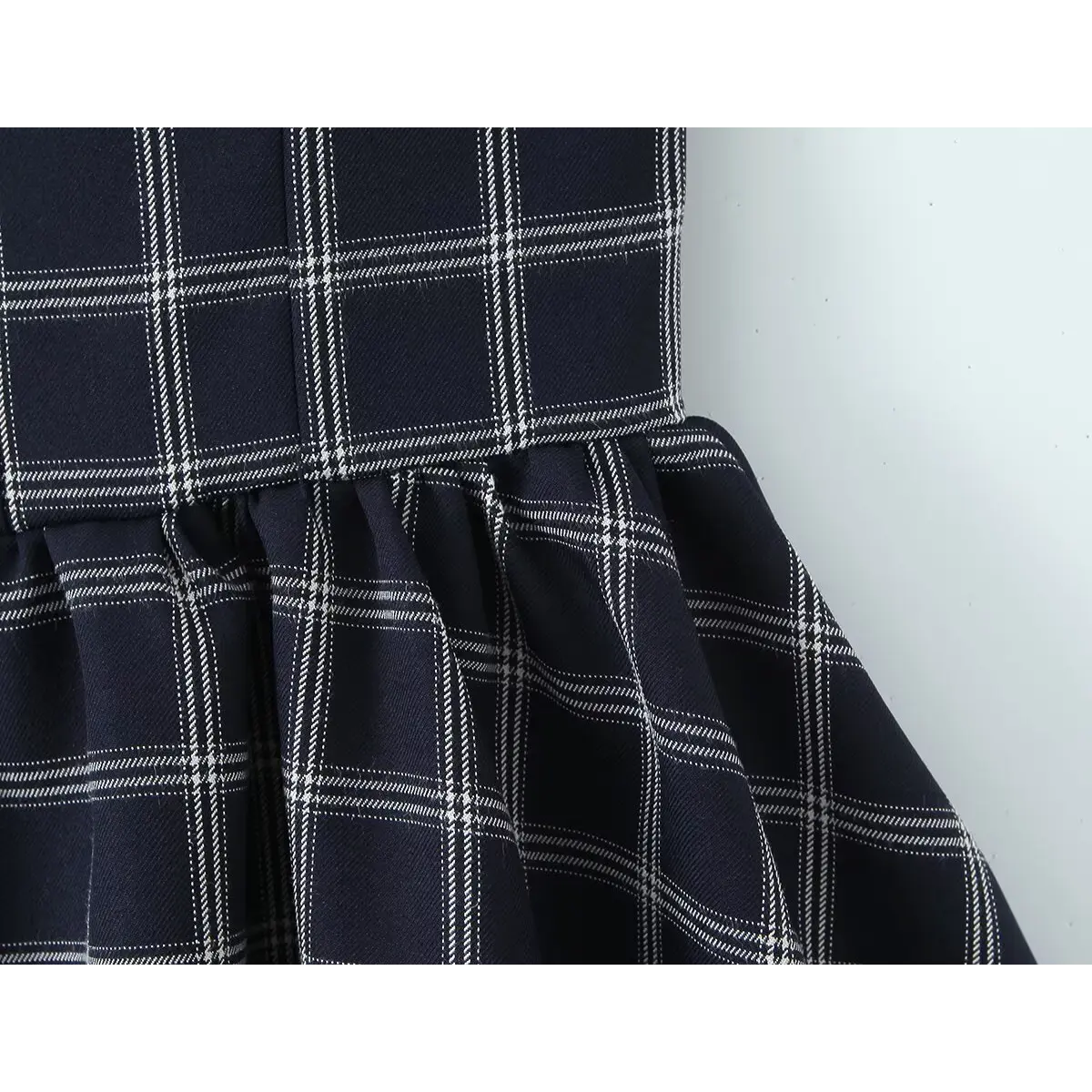 Close-up of the waist seam where the bodice meets the gathered skirt on the navy checkered dress