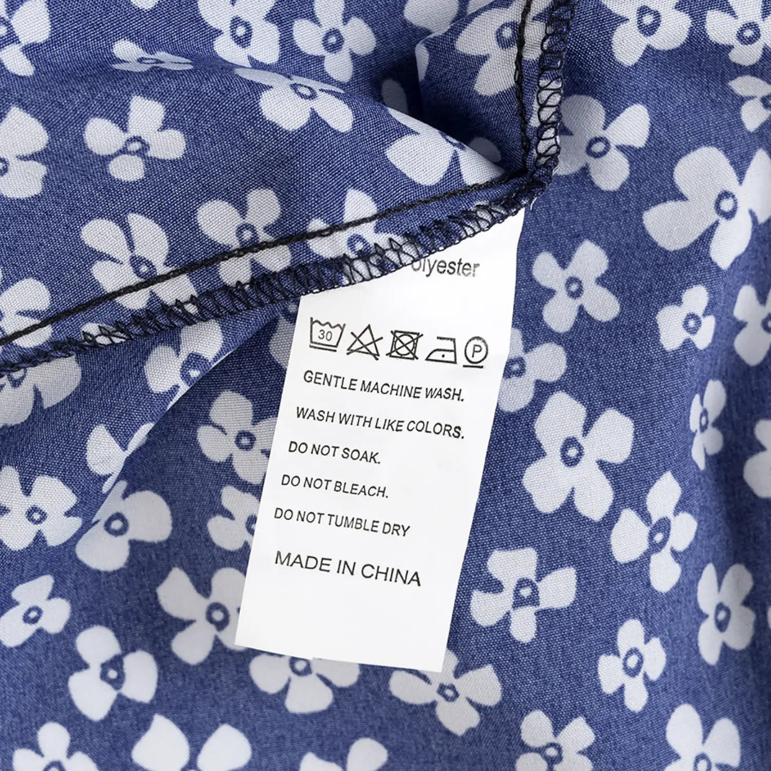 Close-up of the care label on the navy blue floral dress, showing polyester composition and washing instructions