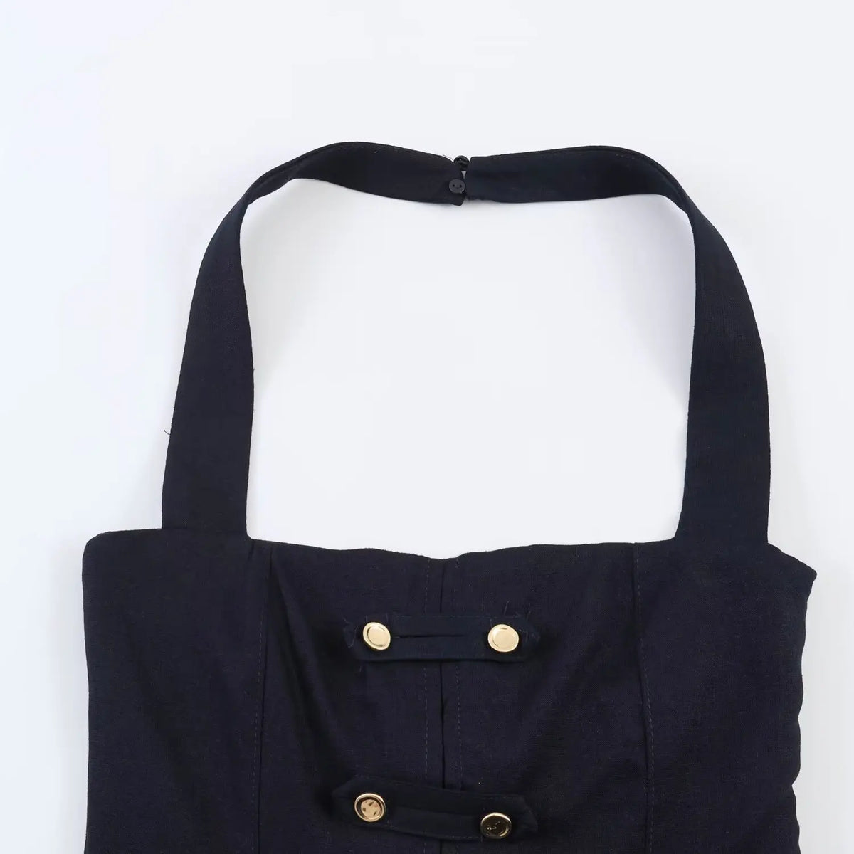 Close-up of gold decorative button details on navy halter mini dress chest, woven fabric texture