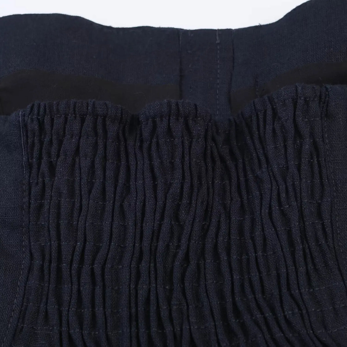 Close-up of smocked elastic back panel on navy halter mini dress, stretch gathered fabric