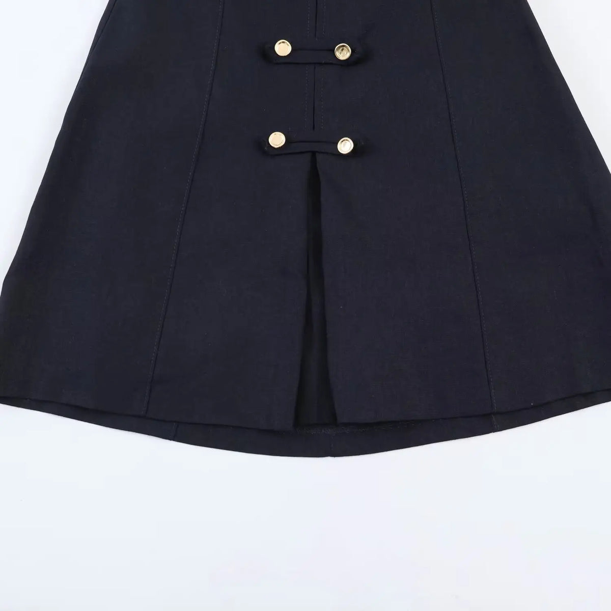 Close-up of skirt hem on navy halter mini dress, decorative gold button tabs and front center slit design