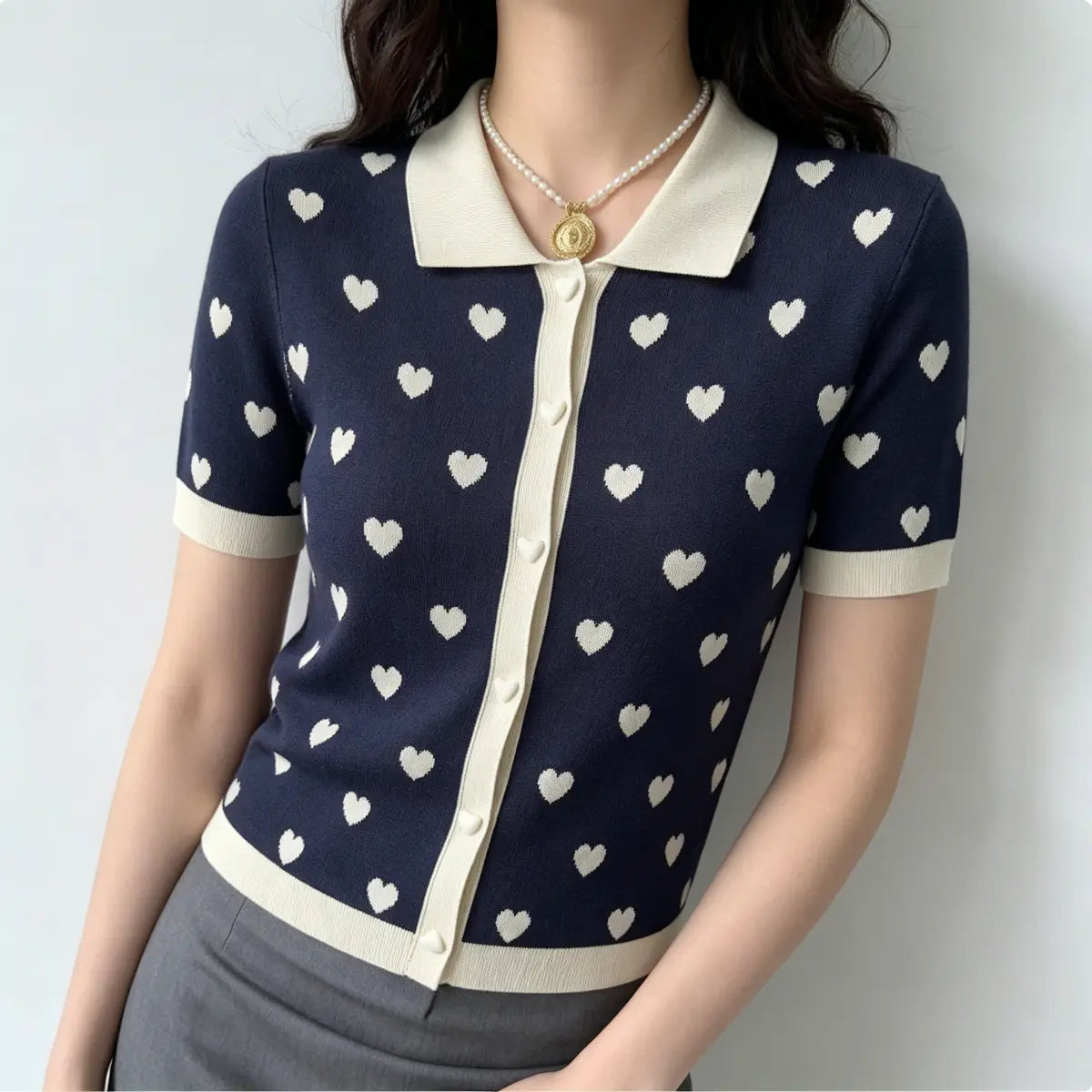 Full view of model in navy heart print knit polo cardigan, paired with grey bottoms for a preppy casual look.