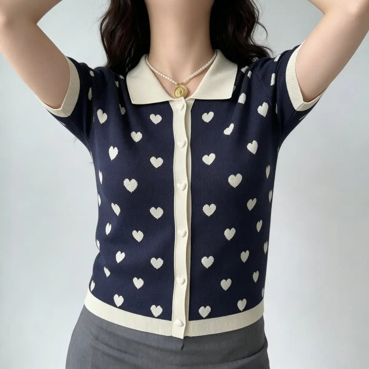 Model with arms raised, wearing navy heart print knit polo cardigan, showing the heart pattern and contrast trim.