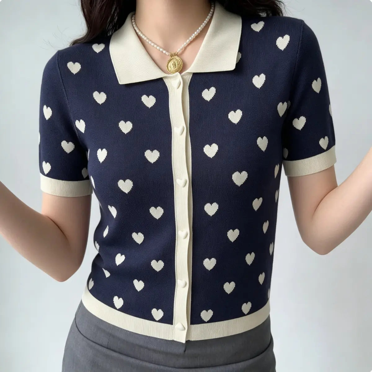 Model with arms raised, showing the fit of navy heart print knit polo cardigan and cream trim details.