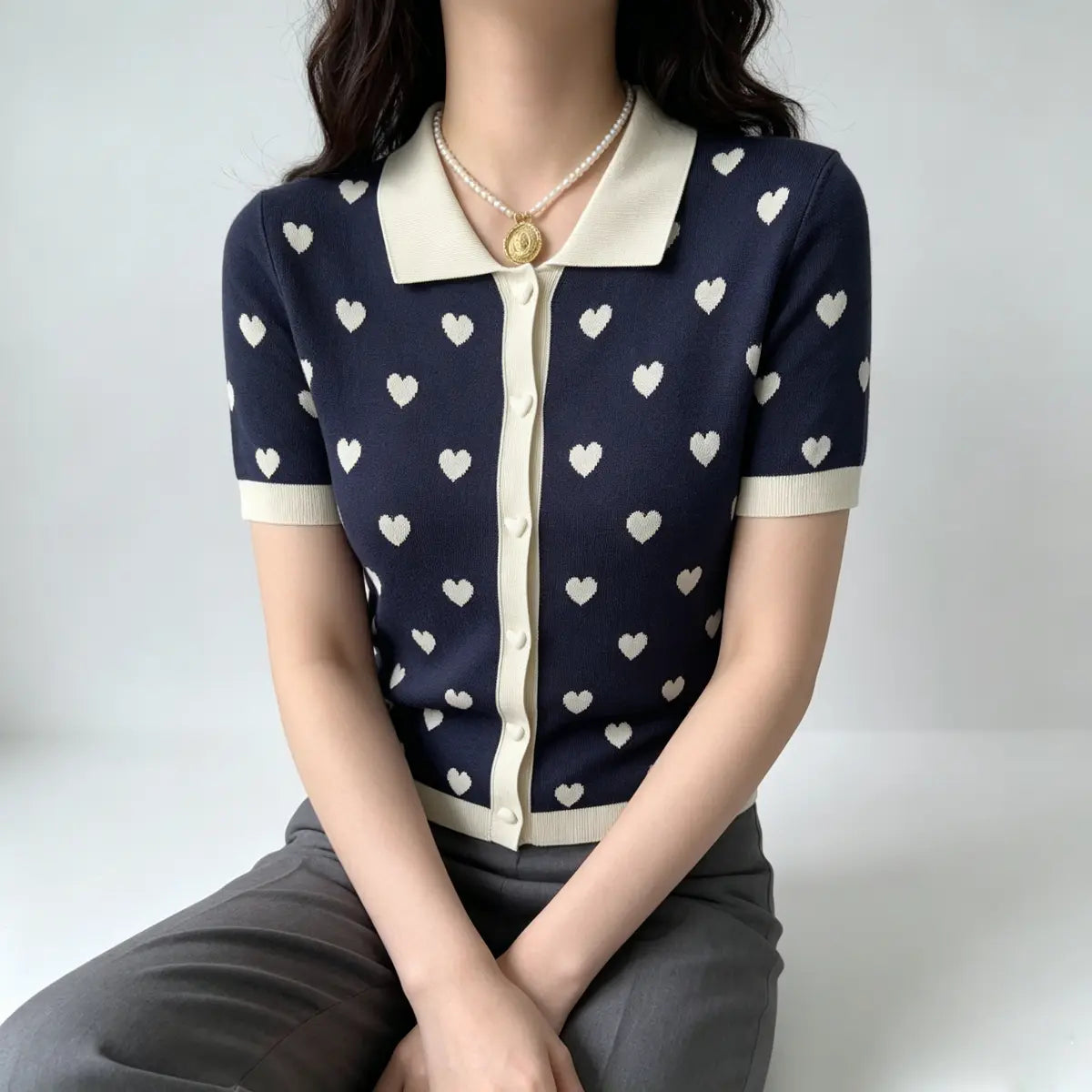 Model seated, wearing navy heart print knit polo cardigan, showcasing the full silhouette and contrast collar.