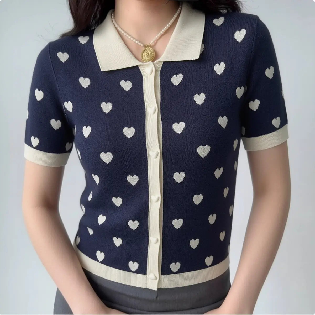 Model wearing navy heart print knit polo top, styled with grey bottoms for a casual preppy look.