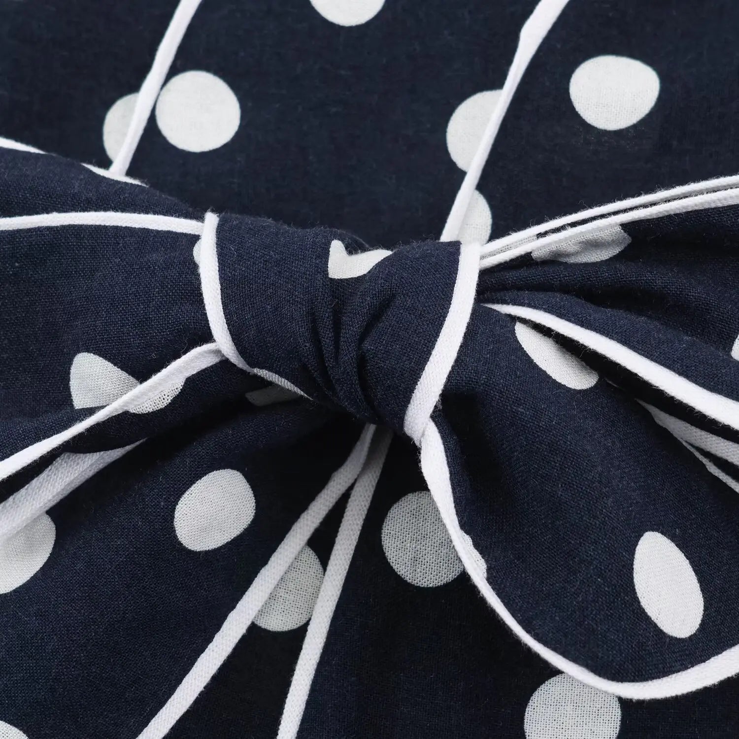 Close‑up of matching waist bow tie with white contrast piping, navy white polka dot fabric, front waist decoration