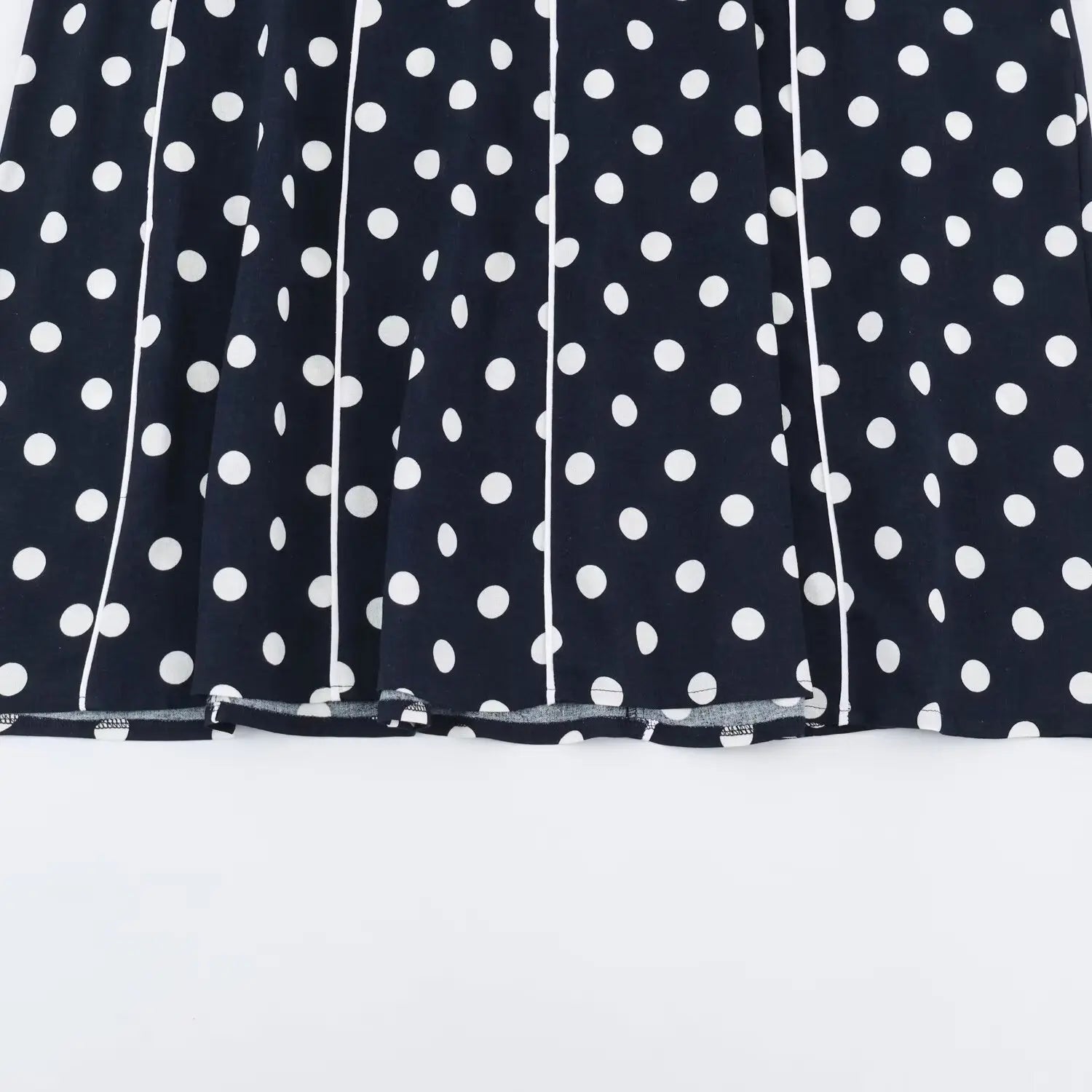 Partial shot of a‑line maxi skirt hem, white contrast piping seams, navy white polka dot print, flowy long skirt panels