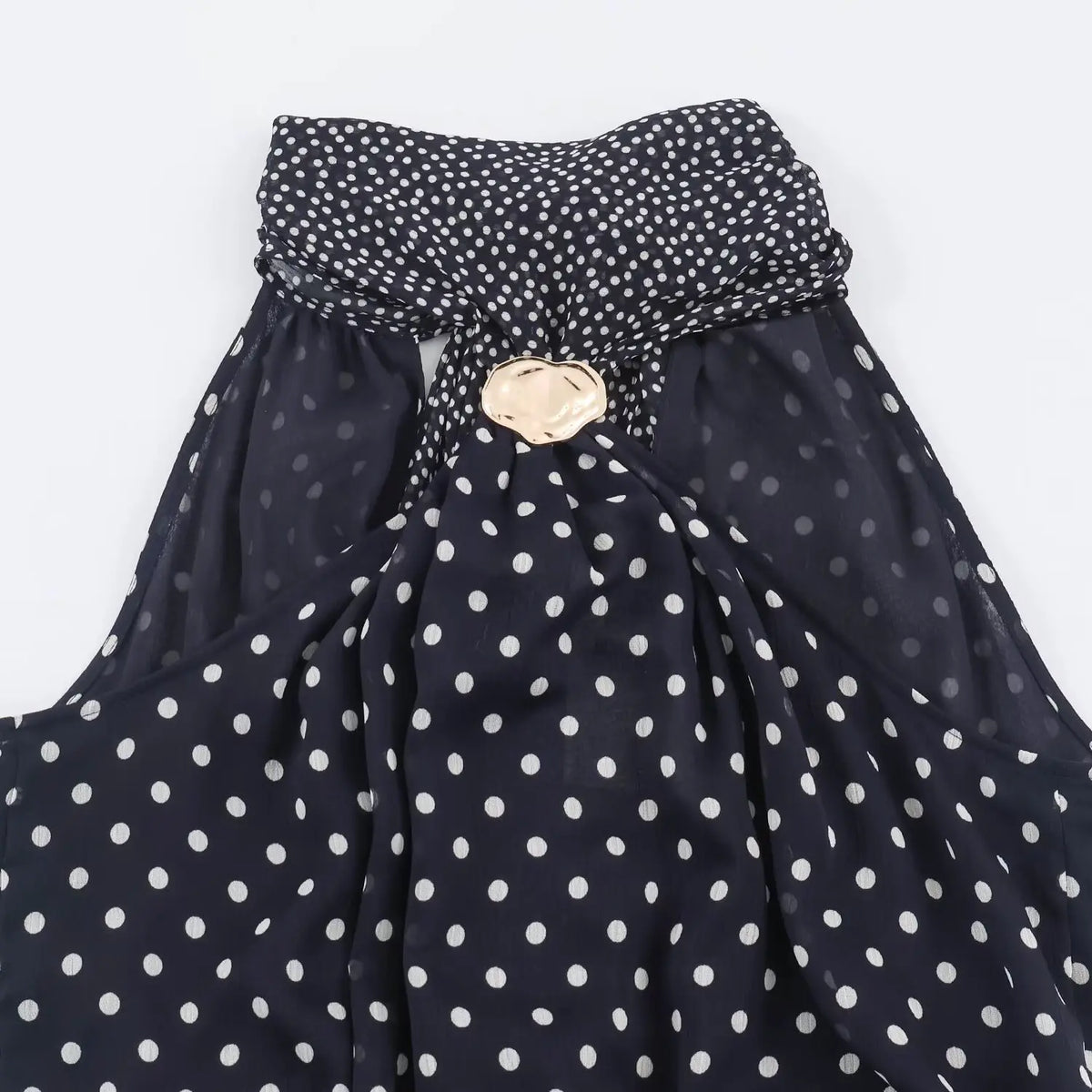 Close‑up of halter neck with gold metal ornament on navy polka dot maxi dress