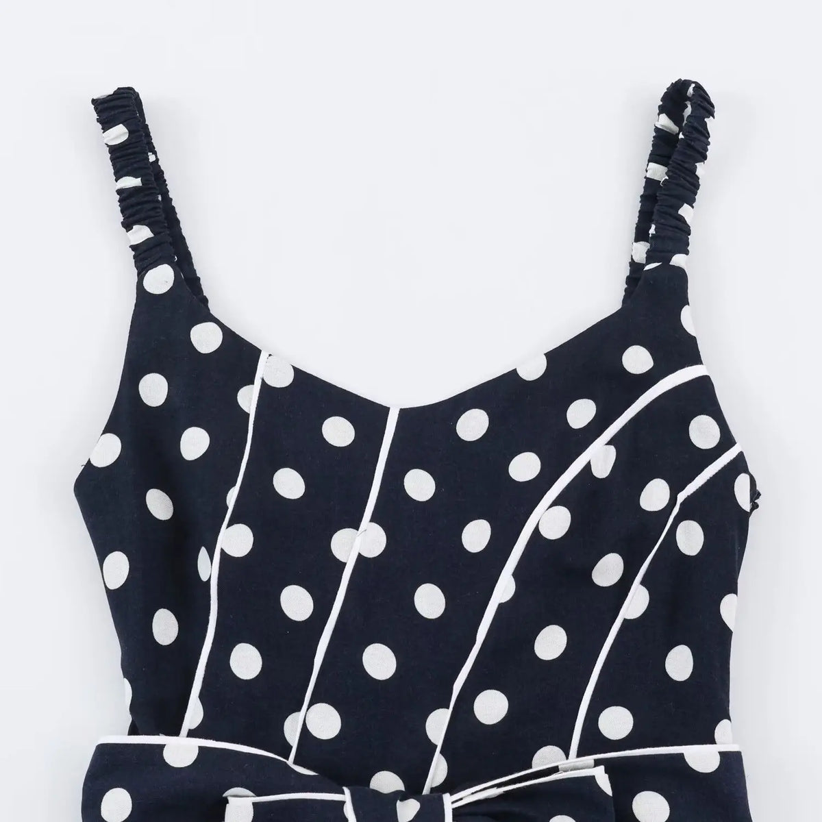 Close‑up of v‑neck bodice, contrast white piping, navy fabric with white polka dot print, smocked strap attachment