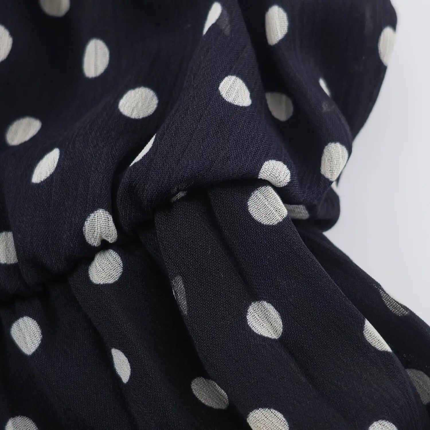 Close‑up of elastic gathered waistband on navy halter polka dot maxi dress