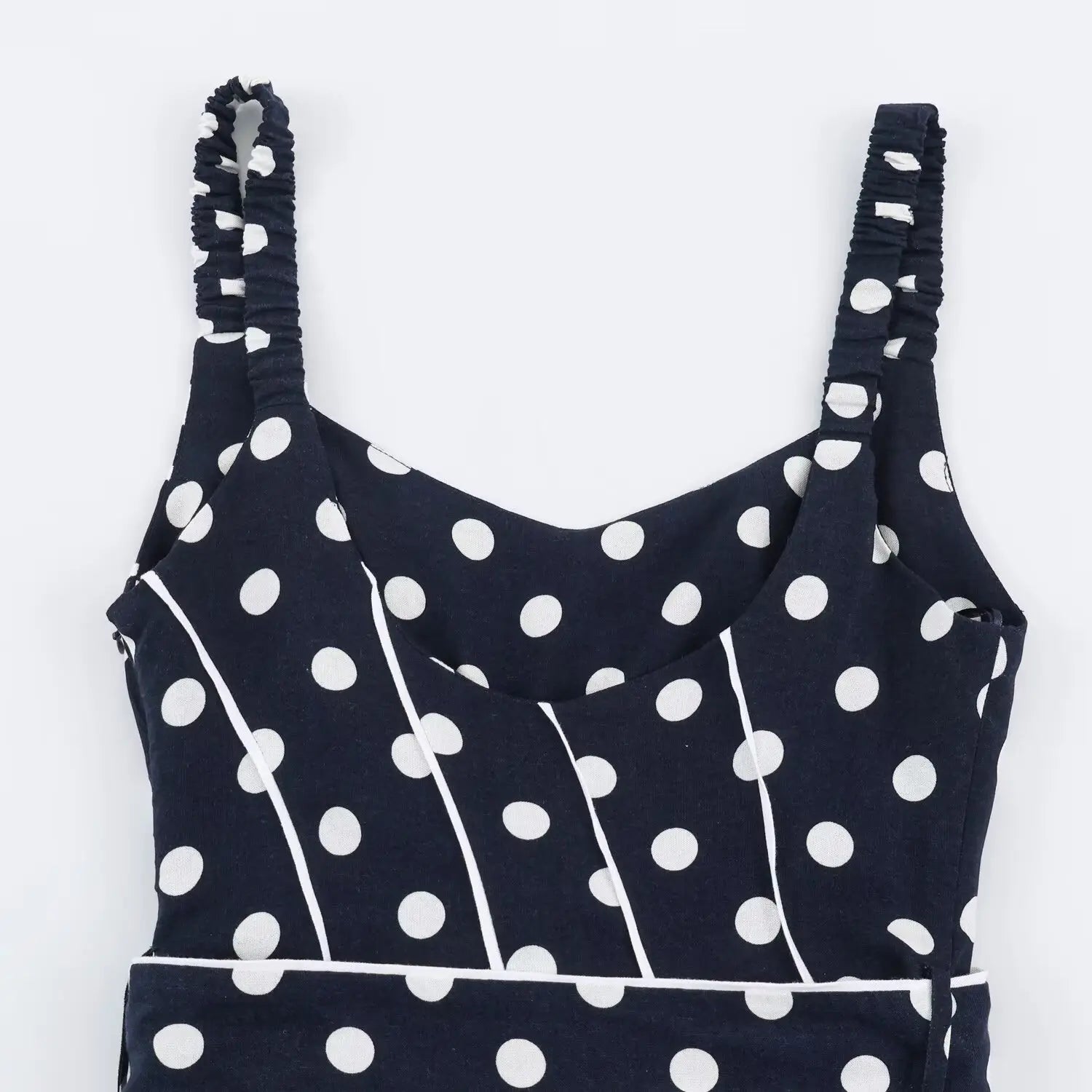 Flat‑lay close‑up of inner back bodice, smocked elastic straps, v‑neck interior, navy polka dot print, contrast white piping seams