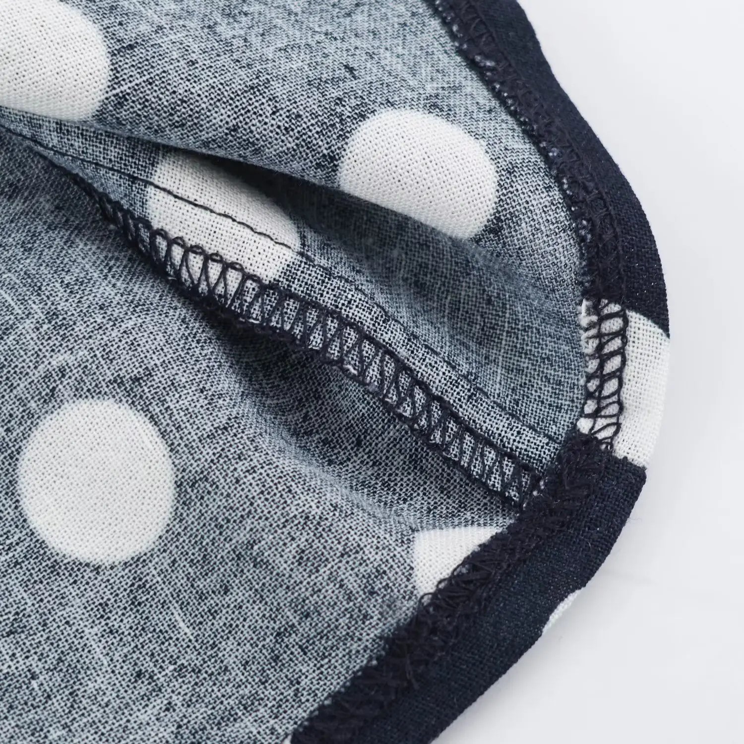 Macro close‑up of inner hem overlock stitching, navy white polka dot woven fabric, neat serged seam finish
