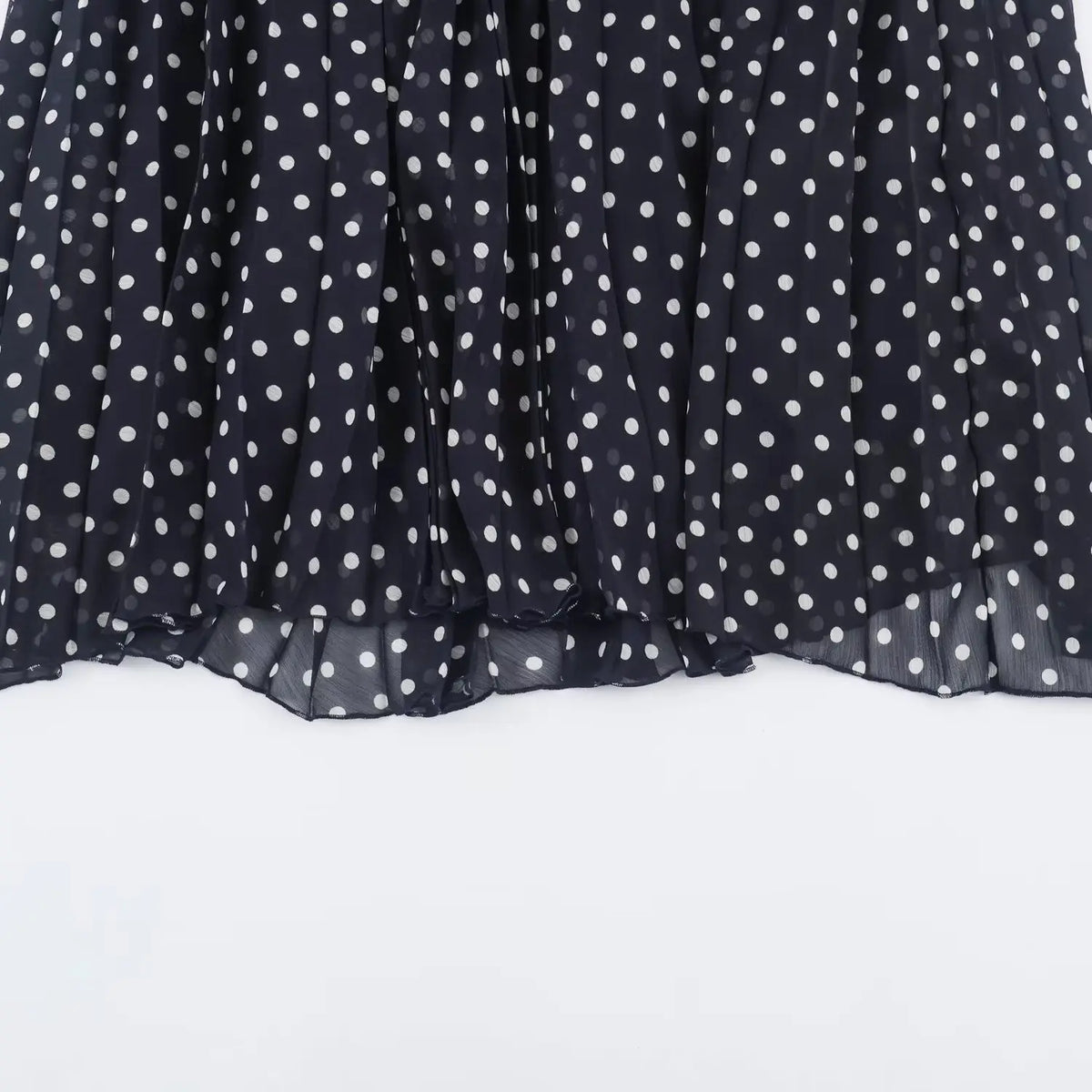 Partial view of full pleated flowy skirt of navy polka dot halter maxi dress