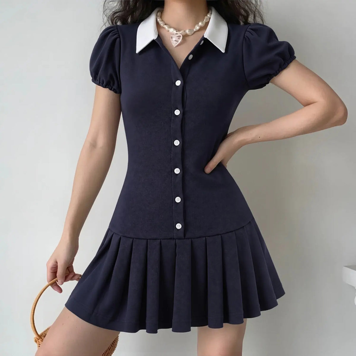 Model wearing navy mini dress with white contrast collar, puff sleeves, button front and pleated skirt