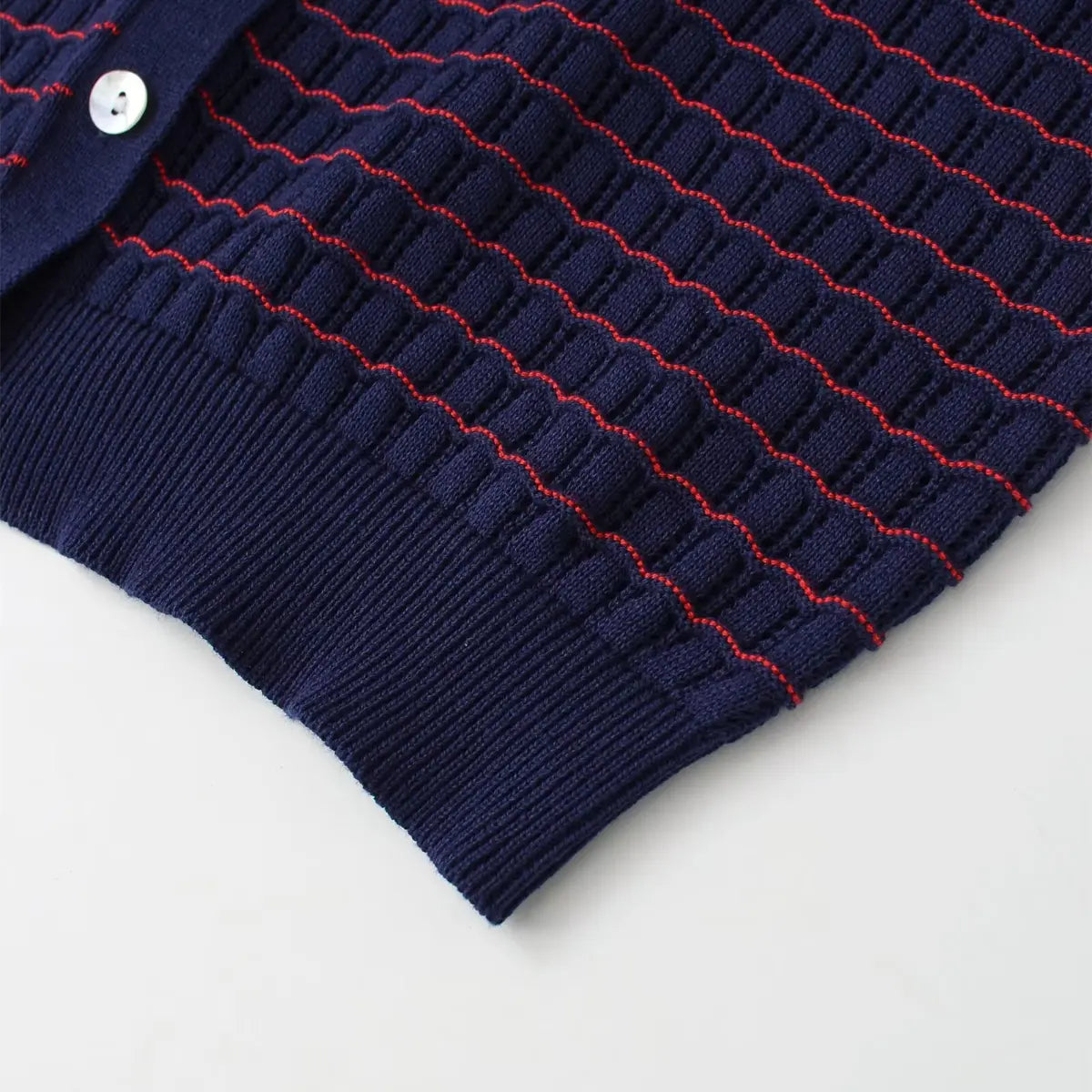 Hem detail of navy and red striped knit cardigan, showing the ribbed hem, openwork texture, and mother-of-pearl button