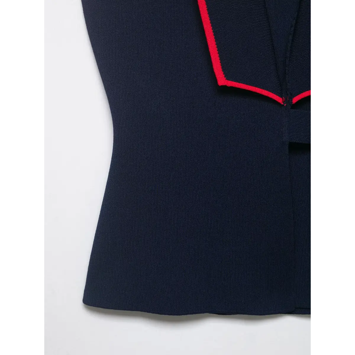 Close-up of the V-neckline and contrast red trim on the navy knit vest