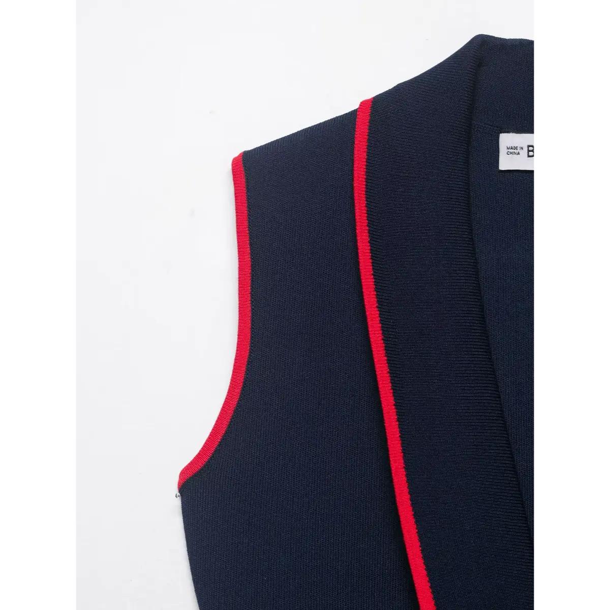 Close-up of the shoulder seam and red contrast piping on the navy knit vest