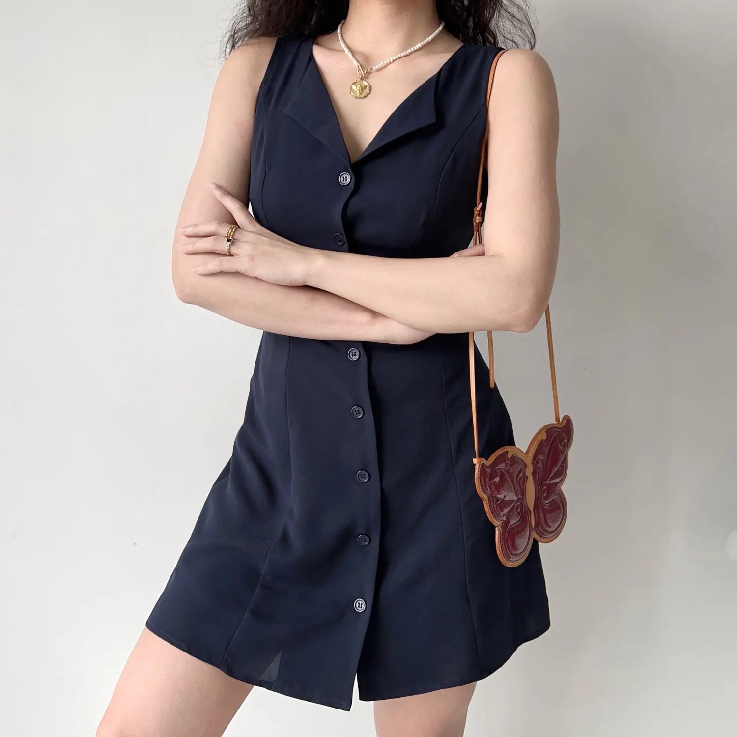 Model front crossed arms pose navy sleeveless notched collar button down mini dress clean tailored silhouette
