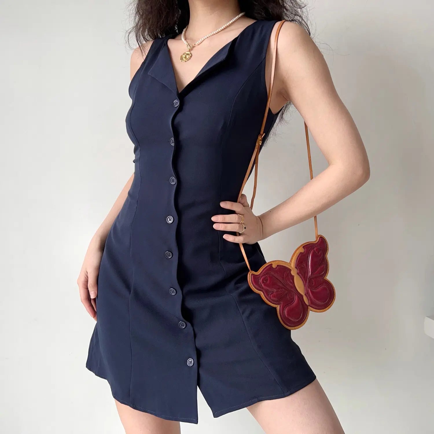 Model front hand on hip pose navy sleeveless notched collar button‑front mini dress tailored fitted short dress