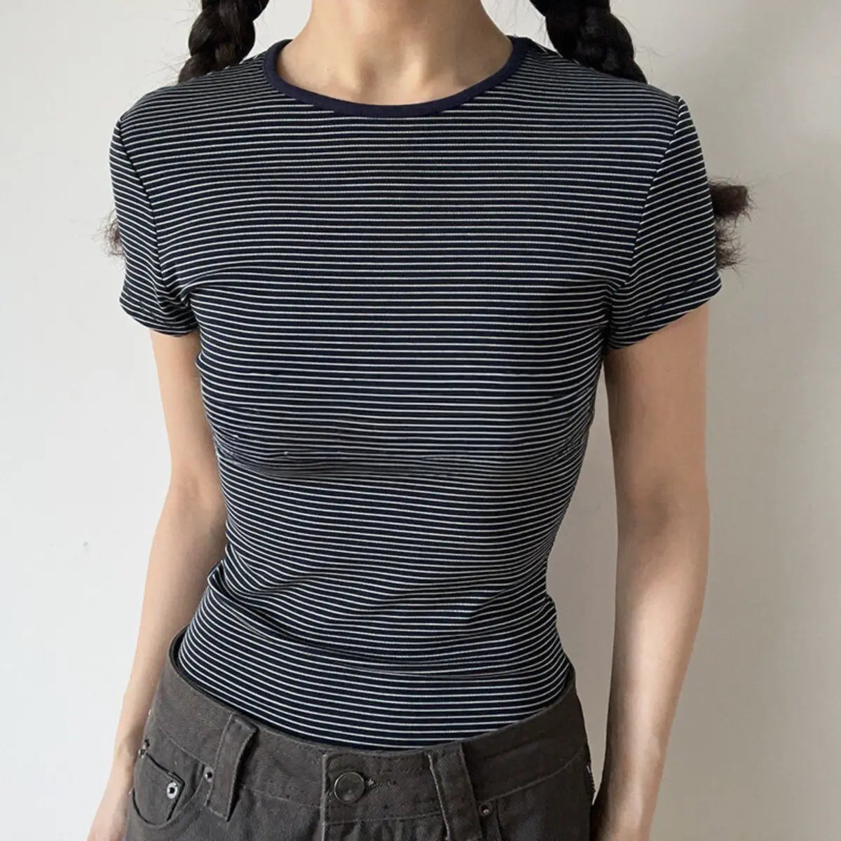  Lifestyle shot of form-fitting navy striped ribbed crew-neck short-sleeve t-shirt, tucked into jeans