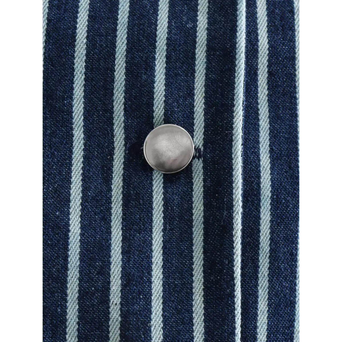 Close-up of the vest's silver metal button on the striped fabric.