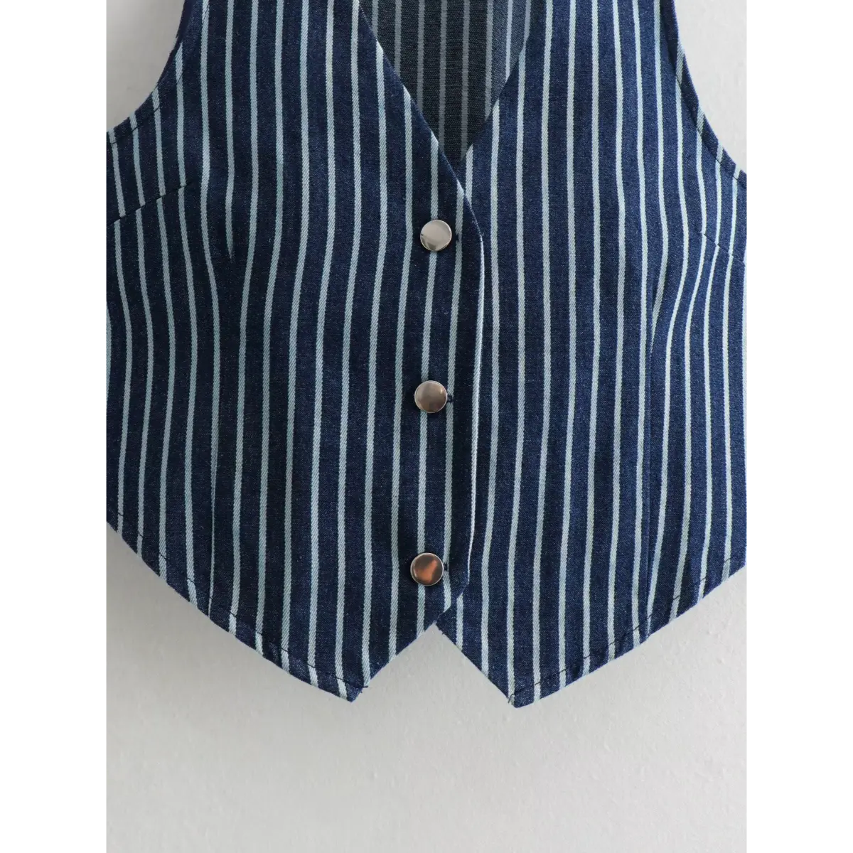 Close-up of the vest's front showing the three metal buttons and V-shaped hem.