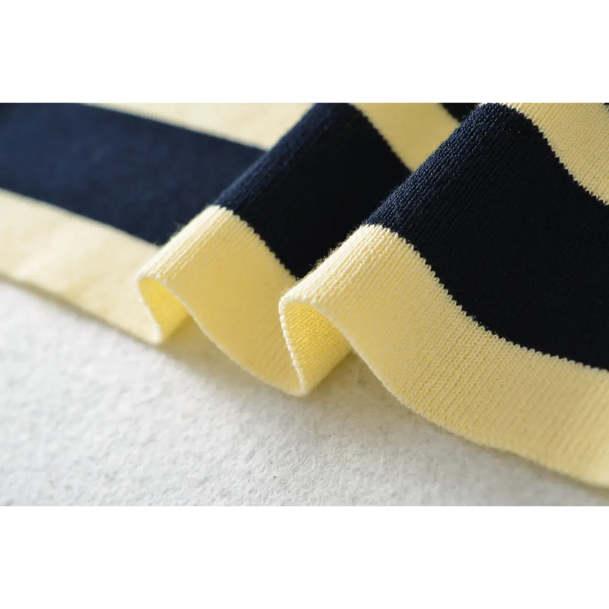 Close-up detail of the finished hem on a navy and pale yellow striped ribbed knit maxi dress, showing the fabric drape and texture.
