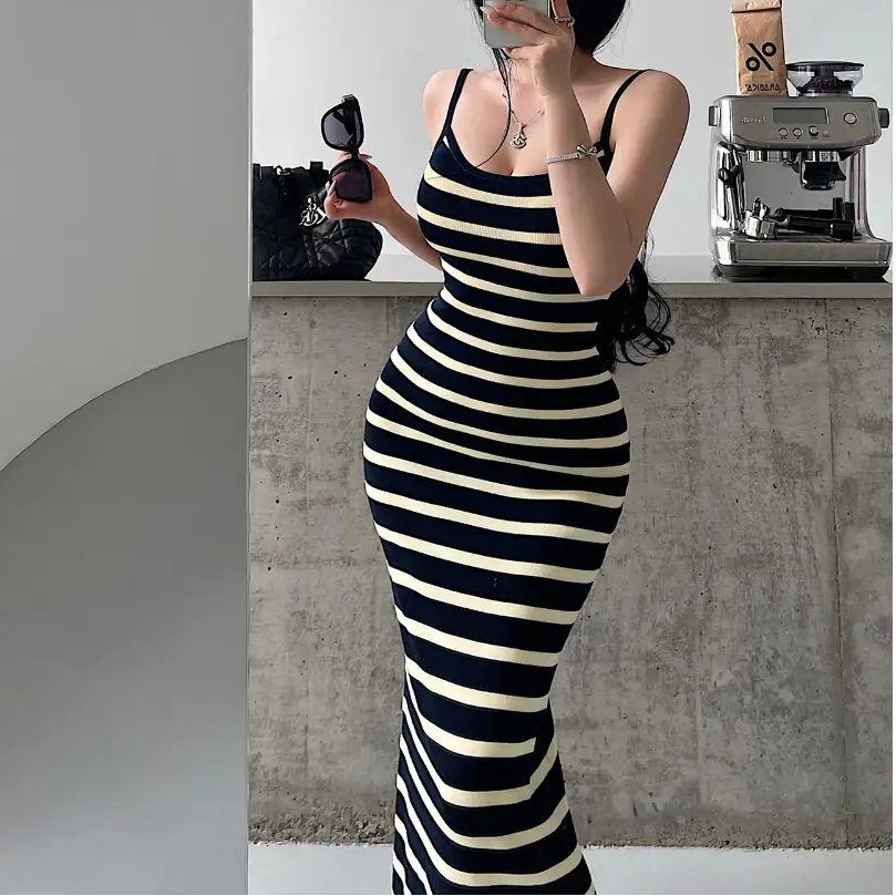 A woman wearing a navy and pale yellow striped ribbed knit maxi dress, styled with accessories, showing the form-fitting silhouette.