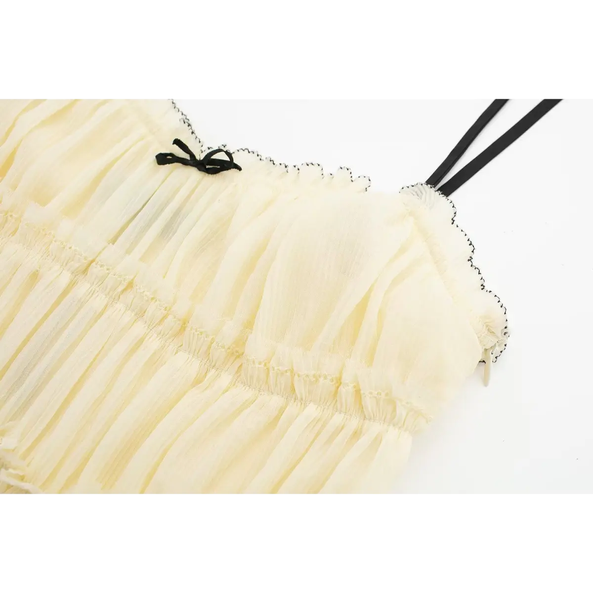 Close-up of the neckline on a cream smocked cami dress, featuring black contrast stitching, a small bow detail, and black spaghetti straps.