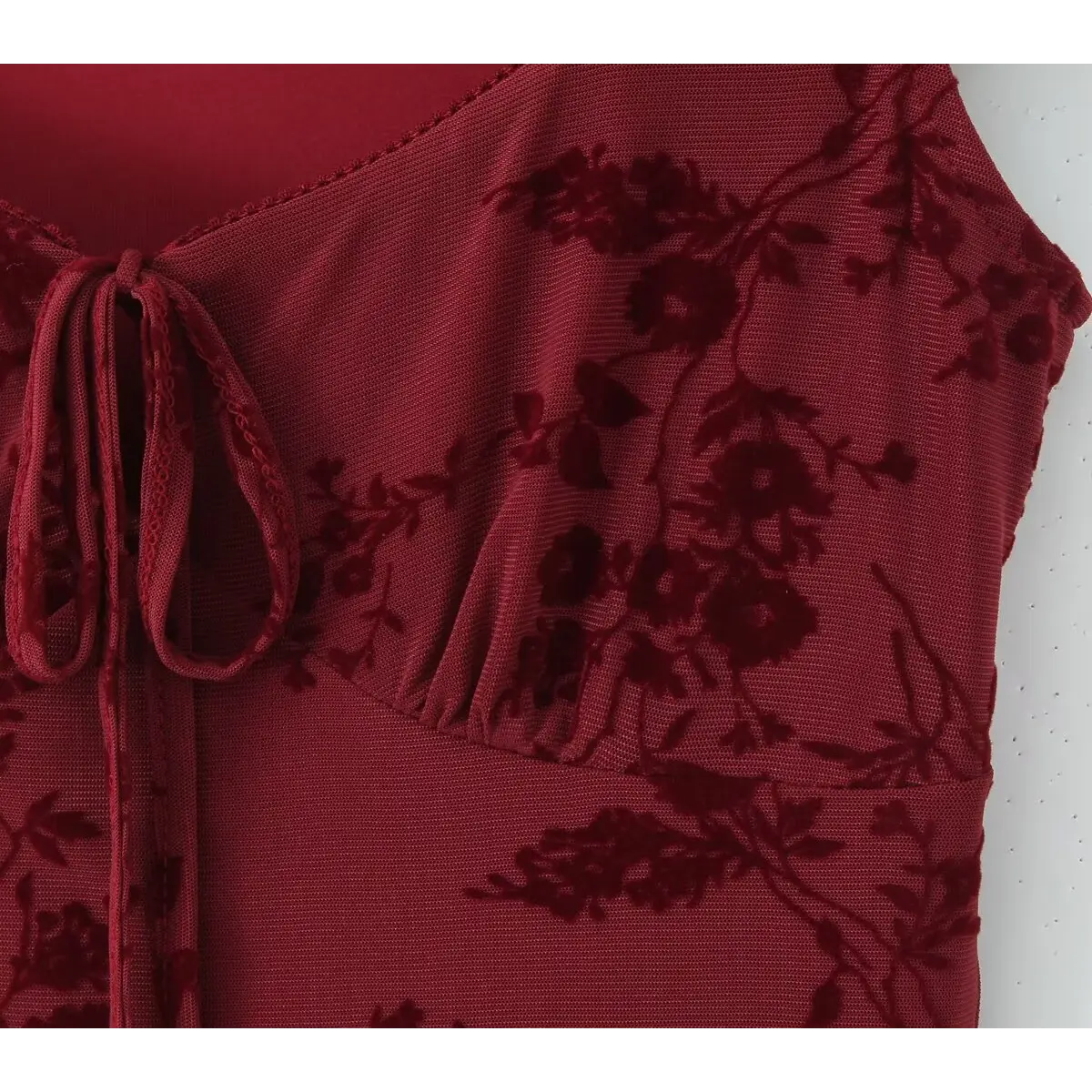 Close-up of the square neckline on a burgundy flocked floral mesh dress, showing the front tie detail and scalloped edge.
