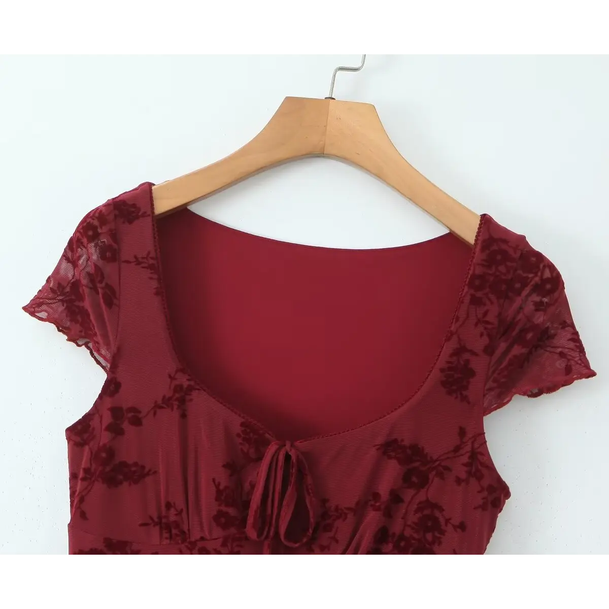 Close-up of the square neckline on a burgundy flocked floral mesh dress, showing the front tie detail and scalloped edge.