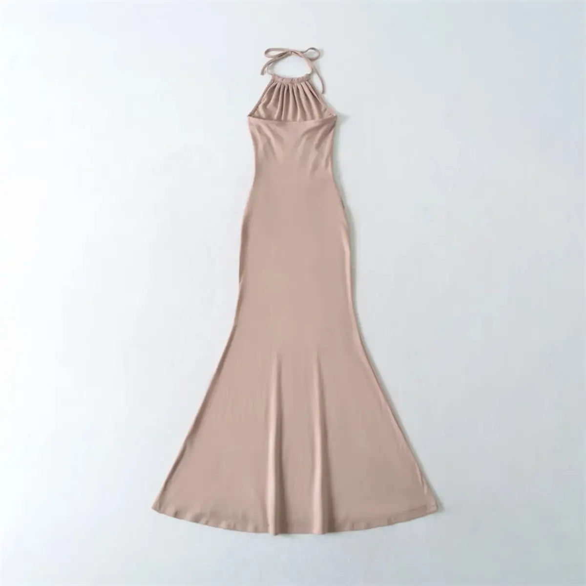  Flat lay back view of a nude halter-neck mermaid maxi dress, showing the tied neck strap and form-fitting silhouette.
