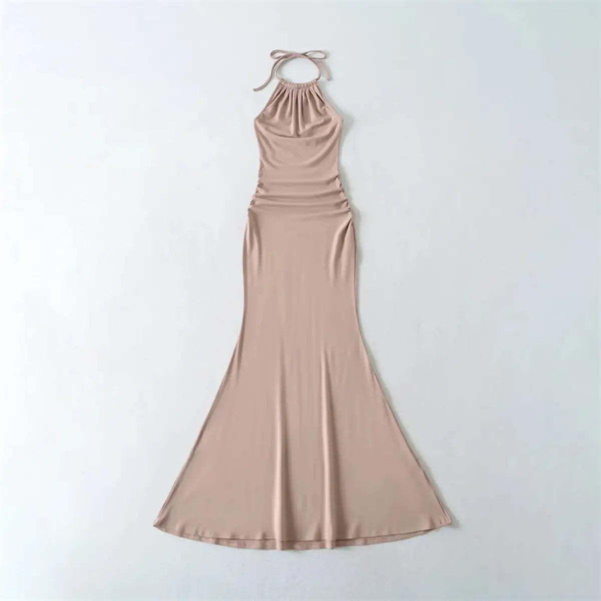 Flat lay view of a nude halter-neck mermaid maxi dress, showing the ruched neckline, tied straps, and ruched waist detail.
