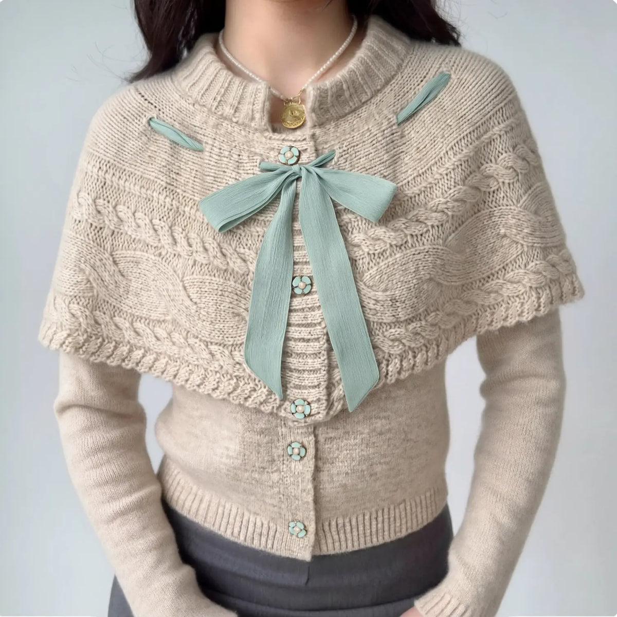 Model wearing oatmeal knit cardigan paired with cable knit capelet, mint green ribbon bow, vintage feminine outfit