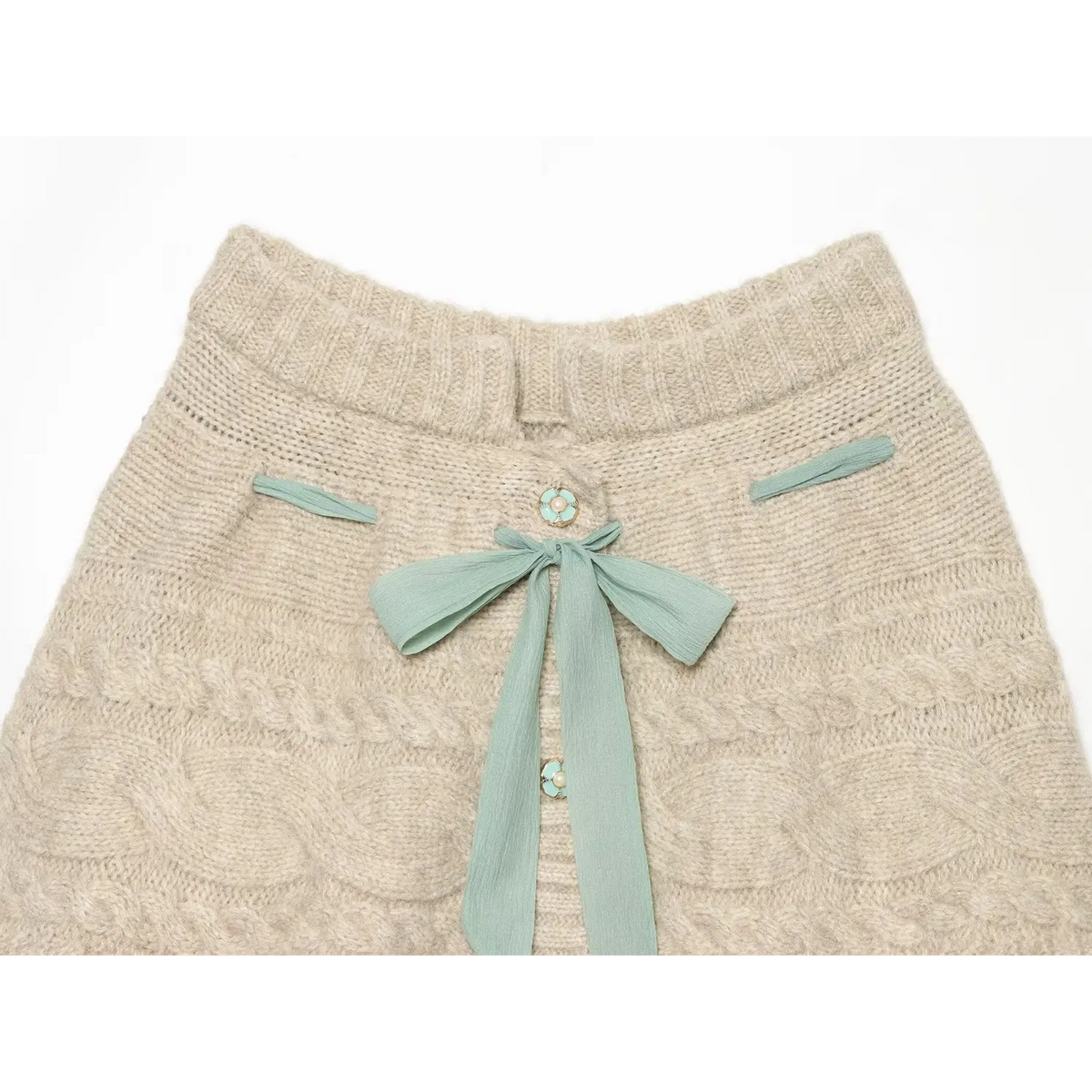 Close up of oat cable knit skort front, featuring mint chiffon bow and flower pearl decorative buttons